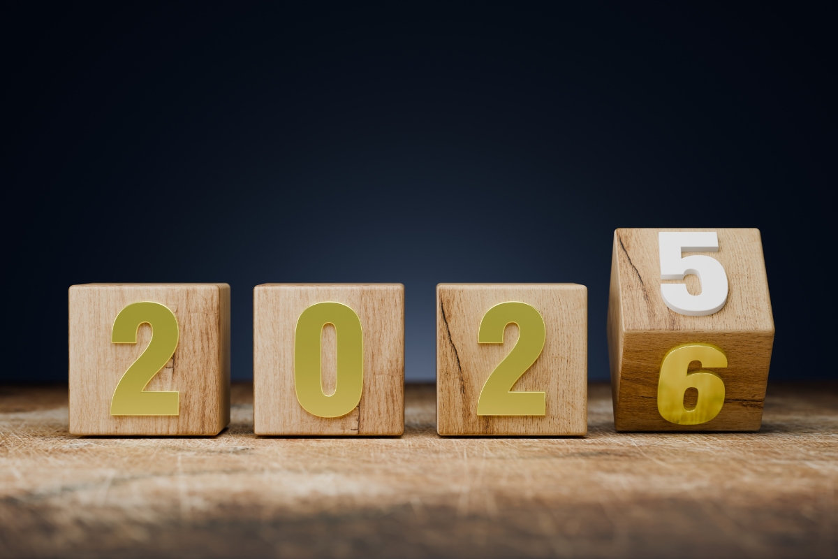Four wooden blocks on a surface; the first three show "202," and the fourth is rotating to change the year from 2025 to 2026.