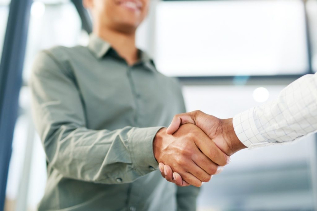 A close-up of two people shaking hands in a bright office setting.