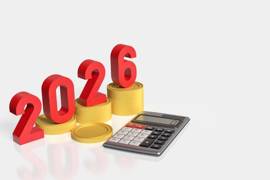 Large red 3D numbers spelling "2026" standing on stacks of gold coins of increasing height, positioned next to a silver digital calculator on a reflective white surface.